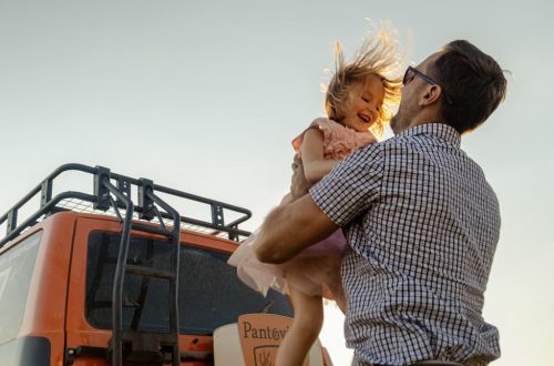 A joyful moment between a father and daughter outdoors with a van in the background.